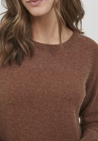 Bruine gebreide trui met een ronde hals, zachte textuur en lange mouwen. Uitgelicht door een subtiele glans en minimale ontwerpelementen.
