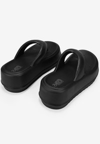 Sandalias de plataforma negras con dos correas anchas y una plantilla texturizada. La suela exterior es lisa y tiene una ligera curvatura en el talón.