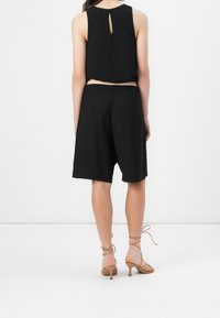 Mustat hihattomat puserot, joissa on avainreikäselkäyksikkö, yhdistettynä polven pituisiin mustiin shortseihin, joissa on sileä pinta ja rento istuvuus.