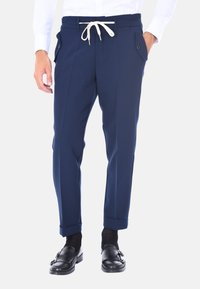 Pantaloni blu navy con vita regolabile, tasche frontali e orli arrotolati, realizzati in tessuto liscio. Abbinati a scarpe nere senza lacci.
