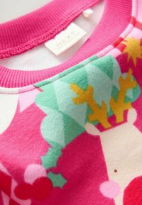 Nahaufnahme eines rosa Kinderpullovers mit geripptem Kragen, der ein Weihnachtsdesign mit einem Rentier und Stechpalmenbeeren zeigt.
