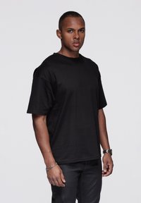 Musta puuvillainen t-paita, jossa on lyhyet hihat ja pyöreä pääntie. Kangas on sileäpintainen, ja se on yhdistetty mustiin housuihin sekä hopeiseen rannekoruun.