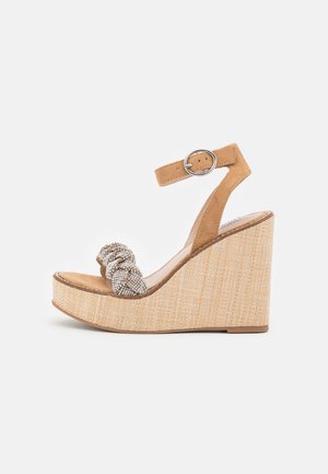 Beżowy sandał na koturnie z paskiem wokół kostki, jasnobeżową teksturowaną podeszwą i ozdobnym, supełkowym wzorem z małymi błyszczącymi dodatkami.