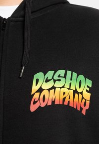 Black zip-up hoodie featuring a bold, gradient logo in green, yellow, and red that reads "DC SHOE COMPANY" across the chest.
