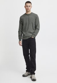 Camisa gris de manga larga con tejido texturizado, cuello redondo, combinada con pantalones negros y zapatillas gris con suelas gruesas y cordones.