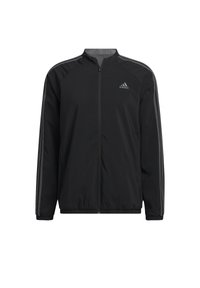 Veste de sport noire avec fermeture éclair sur le devant, comprenant des bandes latérales grises et un logo brodé. Confectionnée en tissu léger et lisse, avec des poignets élastiques.