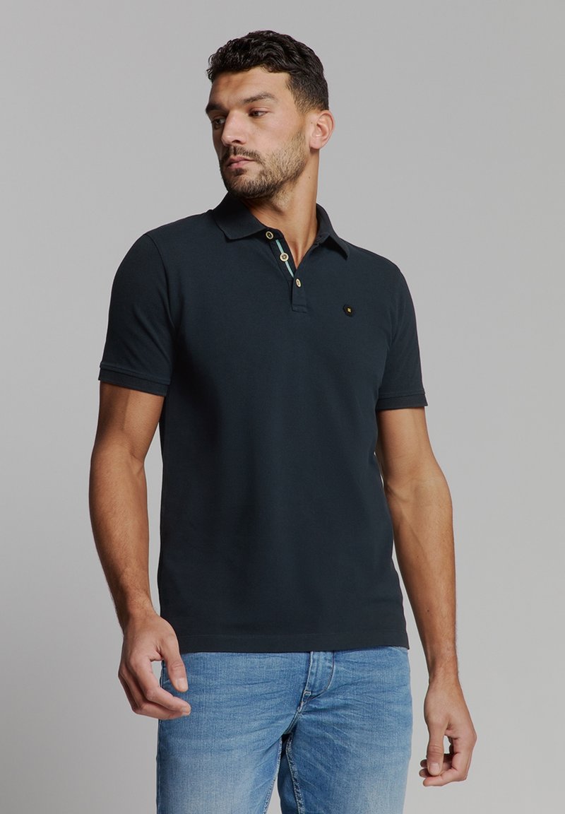 Zwarte polo met een klassieke kraag, gouden knopen en een klein embleem op de borst. Gekocht met lichtblauwe jeans. Gladde katoenen stof.