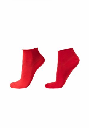 Par de calcetines tobilleros lisos de color rojo brillante mostrados en formas de pie translúcidas sobre fondo blanco.