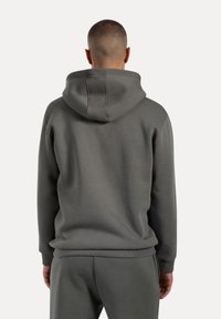 Sudadera gris hecha de tela suave, con una gran capucha, puños y dobladillo acanalados. La vista trasera muestra un diseño sin costuras y un ajuste relajado.