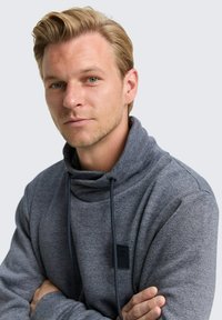 Grijs, geweven sweatshirt met een hoge kraag, trekkoorden en een klein zwart label op de borst. Heeft een ontspannen pasvorm en lange mouwen.