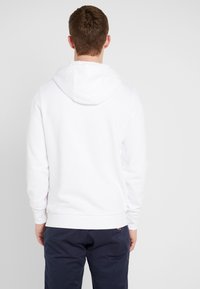 Witte hoodie met een zachte textuur, voorzien van een verstelbare capuchon, geribde manchetten en zoom. De achterkant toont een eenvoudige uitvoering zonder graphics.
