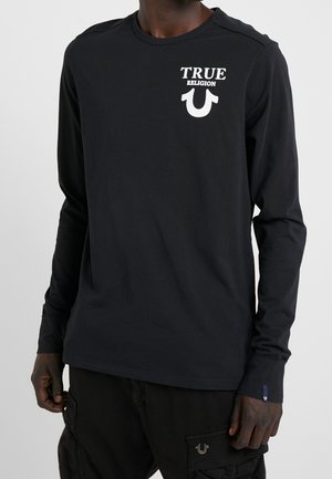 Czarna koszula z długim rękawem wykonana z bawełny, z białym napisem "TRUE RELIGION" i logo podkowy na górnej lewej stronie klatki piersiowej.