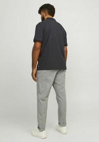 Navy polka dot polo shirt with short sleeves, paired with light gray trousers and white sneakers, viewed from behind.