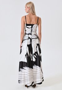 Robe noire et blanche avec un motif floral, fabriquée en tissu lisse. Présente des bretelles fines, un corsage ajusté et une jupe fluide et ample.