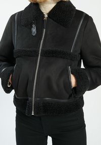 Chaqueta bomber negra con un suave cuello y puños de forro polar, cierre de cremallera y acentos de cuero en contraste a lo largo de las costuras.
