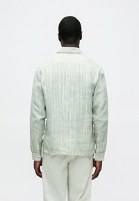 Zöld-fehér csíkos ing, gombos gallér, texturált anyag, hosszú ujjú, testhez álló szabás, látható varrások és finom szegélyrészletezés.