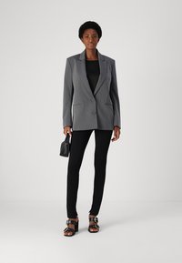 Gray tailored blazer with notched lapels, single button closure, and side pockets, paired with black leggings and open-toe sandals.