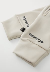 Kreemjad kindad on valmistatud pehmest kangast, millel on must tikandiga "Columbia" logo ja kinnituse detail varruka ääres. Sile tekstuur ja mugav disain.