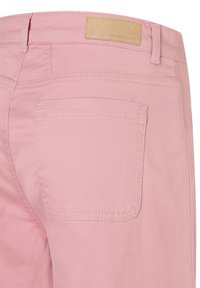 Close-up of pink denim jeans showing back pocket, belt loops, and beige leather brand patch reading "MORE & MORE."