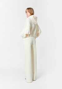 Sudadera con capucha de color crema con mangas rizadas, combinada con pantalones anchos a juego. Tejido suave, corte relajado, diseño minimalista.
