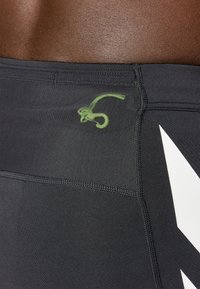 Black athletic shorts made of smooth fabric, featuring a green logo detail and white graphic accents. Finely stitched seams enhance durability.