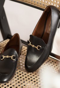 Sorte læder loafers med en glat tekstur, der har en hardwareaccent i guldfarve og et rundt tådesign.
