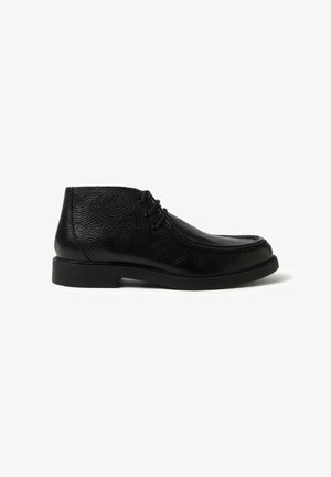 Botín chukka de cuero negro con acabado texturizado, diseño de cordones, puntera redondeada y suela de goma baja y resistente.