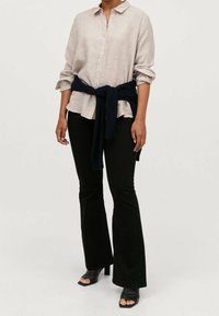 Ljusbeige linne skjorta med uppvikta ärmar, kombinerad med höga svarta utsvängda byxor. En marinblå tröja är knuten i midjan. Svarta klackar med öppen tå.