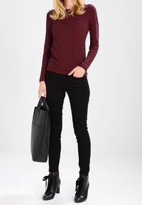 Blusa de manga larga en color burdeos, jeans ajustados negros, botas negras de tobillo con cordones y un bolso negro. Texturas suaves y un diseño ajustado.