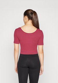 Korte ermers, ribbestrikket crop-top i dyp burgunder med en rund hals og en tettsittende design, kombinert med svarte leggings.
