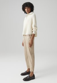 Cream ribbed sweater with a collar, beige suede pants, and dark brown loafers. Soft texture and relaxed fit throughout the outfit.