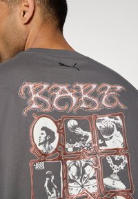 Szary bawełniany t-shirt z wyraźnym czerwonym napisem „RARE” oraz czarnymi grafikami związanymi z koszykówką na plecach. Logo Puma przy kołnierzu.