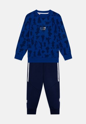 Felpa blu con motivi a silhouette, scollo rotondo e polsini a costine. Pantaloni abbinati blu scuro con strisce bianche laterali e gambe affusolate.