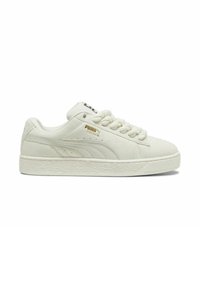 Baskets en suede blanche avec semelle en caoutchouc texturée, bout arrondi et empeigne à lacets. Présente un logo doré sur le côté et un accent noir sur la languette.
