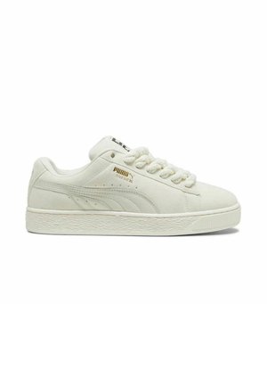 Baskets en suede blanche avec semelle en caoutchouc texturée, bout arrondi et empeigne à lacets. Présente un logo doré sur le côté et un accent noir sur la languette.
