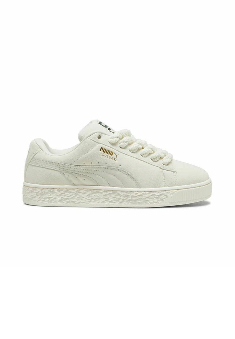 Baskets en suede blanche avec semelle en caoutchouc texturée, bout arrondi et empeigne à lacets. Présente un logo doré sur le côté et un accent noir sur la languette.