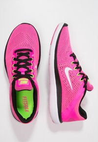 Le sneakers Nike presentano una tomaia in mesh rosa brillante, lacci neri e il logo swoosh bianco. Suola imbottita con accenti verdi e dettagli testurizzati.