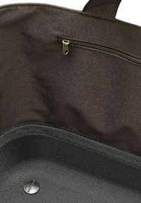 Interior de bolsa de tela marrón con un bolsillo con cremallera y un botón de presión metálico; presenta material texturizado y detalle de borde cosido.