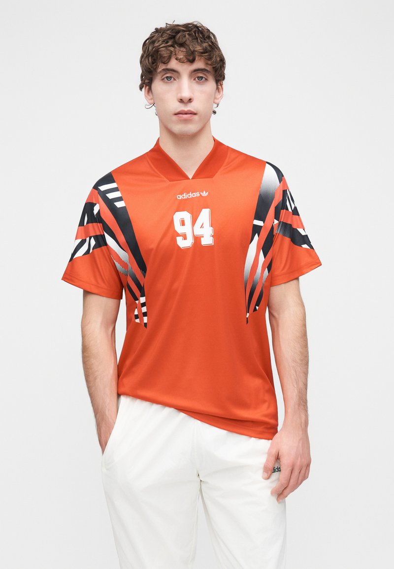 Maillot de sport orange avec motifs abstraits noirs et blancs, manches courtes, col en v, arborant le numéro "94" et le logo adidas sur le devant.