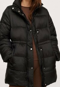 Giacca puffa nera con colletto alto, bottoni a pressione e design trapuntato. Presenta una texture morbida e una vestibilità comoda. Adatta per il freddo.