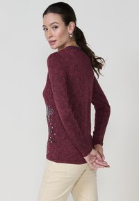 Bordo garās piedurknes T-krekls ar strukturētu apdari, kas rotāts ar ziedu izšuvumu un metāliskiem akcentiem sānos.