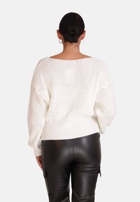 Weißer gestrickter Pullover mit lockerer Passform, schulterfallenden Ärmel und geripptem Saum, kombiniert mit schwarzen Kunstlederhosen. Detaillierte Textur sichtbar.