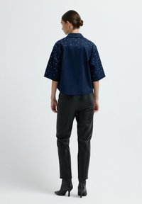 Camicia blu navy a maniche corte con colletto, adornata con decorazioni a pois bianchi sulle spalle, abbinata a pantaloni in ecopelle neri e tacchi.