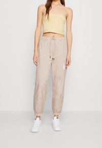 Béžové kalhoty na stažení vyrobené z lehké tkaniny, s elastickými manžetami a decentním logem, kombinované s přiléhavým žlutým topem.