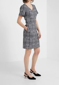 Robe cintrée à manches courtes avec un motif à carreaux bleu marine et blanc, dotée d'un décolleté en V, de deux poches et d'une fermeture éclair à l'avant. Associée à des escarpins noirs à bride arrière.