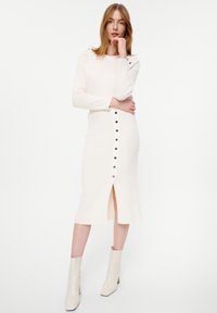 Romana ribgebreide jurk met lange mouwen, voorzien van een voorknopsluiting en een hoge split, gecombineerd met lichte enkelboots.