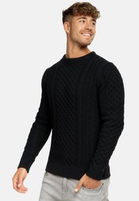 Schwarzer Kabelstrickpullover mit strukturierten Mustern und gerippten Bündchen. Rundhalsausschnitt und figurnah geschnitten, aus dickem Strickmaterial gefertigt.