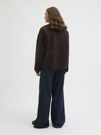 Prune tekstuuriga fliiskate, millel on vaba lõige, kantuna tumedate laia säärega teksade peal, näidates ribakute mansette ja ümmargust kaelust.