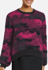 Suéter de punto fuzzy en rosa y negro con patrones abstractos, cuello redondo y puños y dobladillo acanalados, con un diseño de corte relajado.