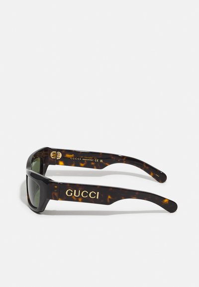 Occhiali da sole tartarugati con una montatura spessa e rettangolare. Logo "GUCCI" in oro sulle aste, lenti scure e finitura lucida.